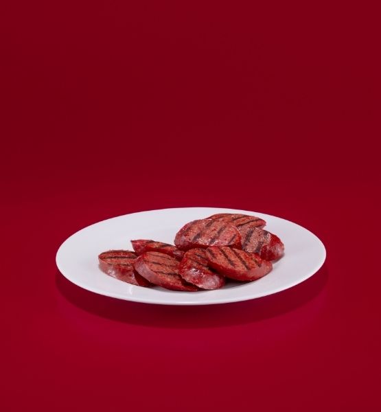 Saucisses grillées disposées sur une assiette blanche sur fond rouge