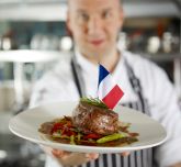 A chef holding a plate with meat and a mini French flag stuck in it
