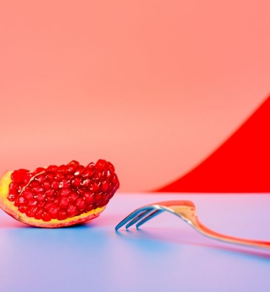 Pomegranate slice on a colorful surface with a metal fork.