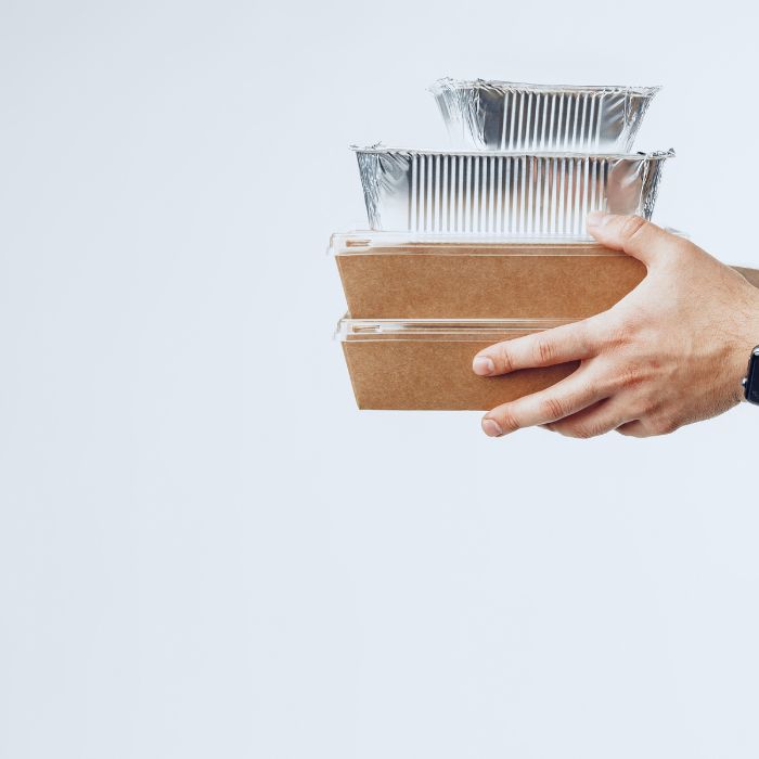 Main tenant des boîtes alimentaires en carton et en aluminium pour emporter, sur fond blanc