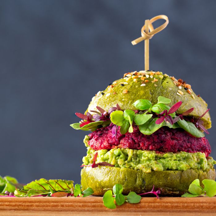 Vegan beetroot burger with green bun, avocado, and sprouts on a dark background.