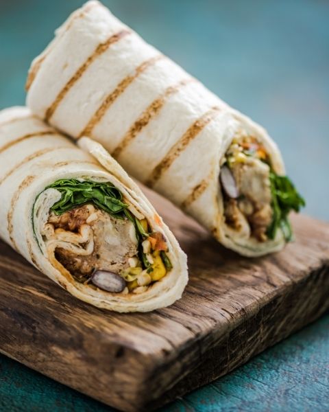 Grilled vegetarian wraps with vegetables and meat on a wooden board.
