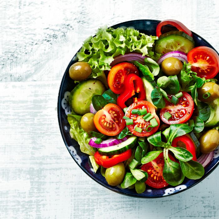 Fresh vegetable salad with tomatoes, cucumber, peppers, olives, and lettuce in a bowl.