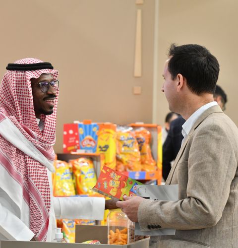 Two professionals talking at a food industry booth, standing in front of colorful packaged products.