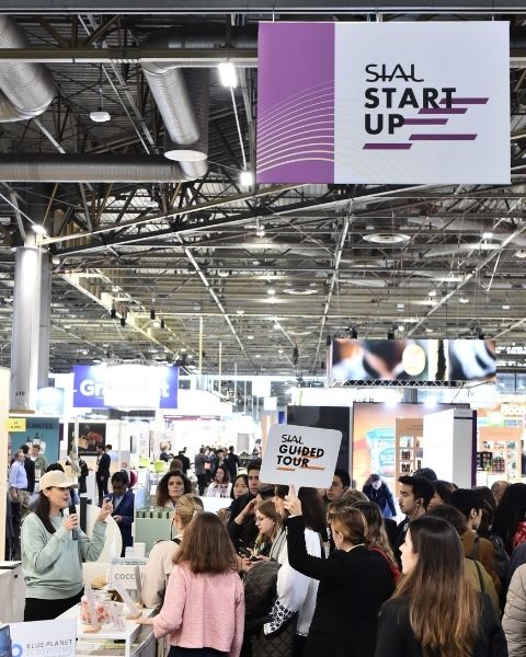 View of the SIAL Start-up booth with a presenter showcasing a product to the public, with a 'SIAL Guided Tour' sign