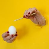Deux mains tenant un œuf blanc et une baguette, émergeant d'un mur jaune vif