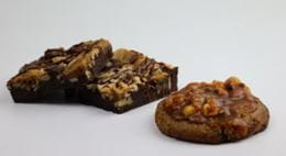 Two plant-based desserts presented on a white surface: a nut brownie and a cookie topped with dried fruits.