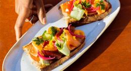 Toasts topped with smoked salmon and fresh vegetables on a plate, hand adjusting the garnishes.