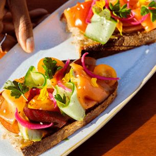 Toasts topped with smoked salmon and fresh vegetables on a plate, hand adjusting the garnishes.