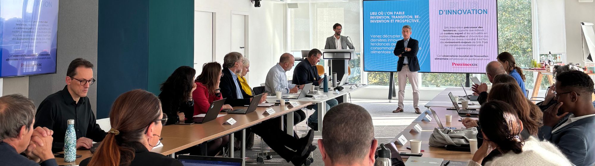 Grand jury of SIAL Innovation 2024 in the middle of deliberation, with experts and jurors around a table, and a presentation on food innovation displayed in the background