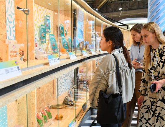 Three women closely observe food products displayed behind a glass showcase.