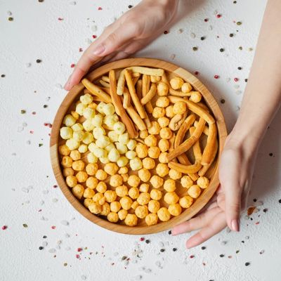 Assiette en bois avec des boules de fromage et des bâtonnets, tenus par des mains.