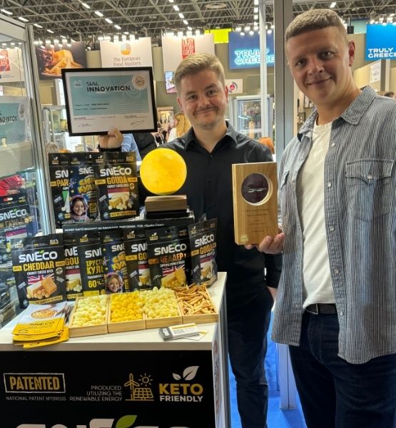 Two people holding trophies and products displayed at their stand, awarded for innovation.