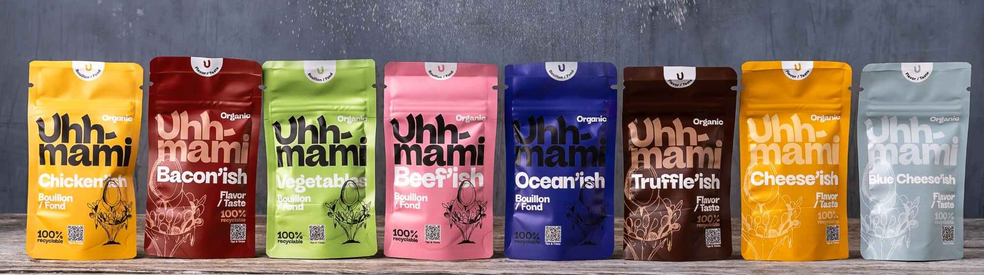 Uhhmami plant-based bouillon pouches displayed on a wooden shelf, featuring various colorful flavors.
