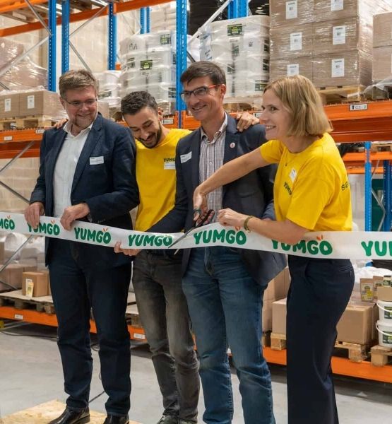 Quatre personnes souriantes coupant un ruban YUMGO lors d’un événement en entrepôt.