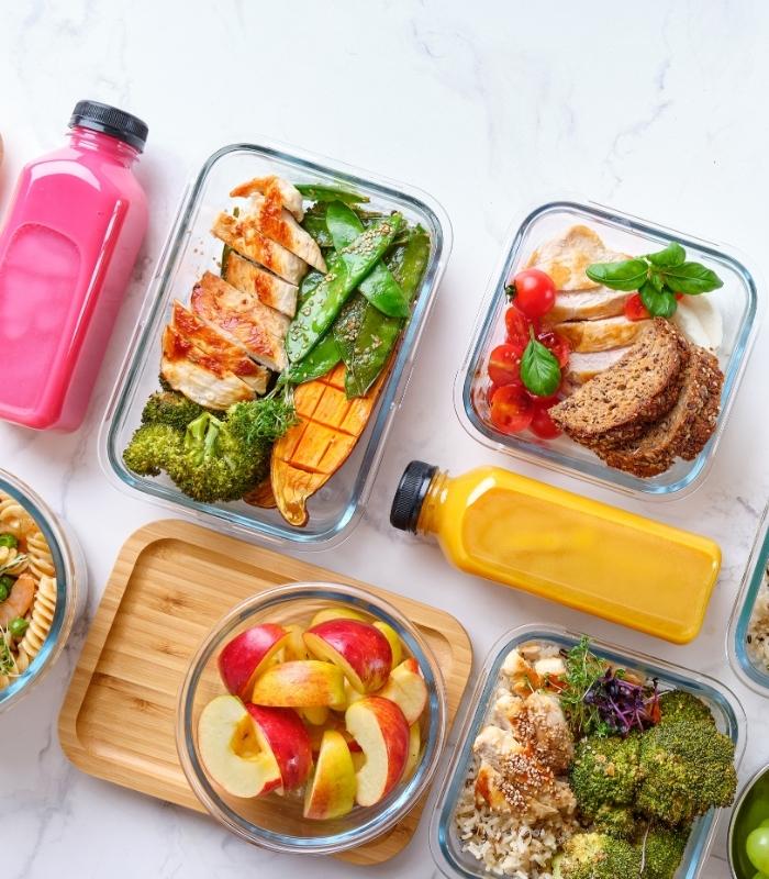 Boîtes repas équilibrées avec poulet, légumes, fruits et boissons colorées sur une table claire