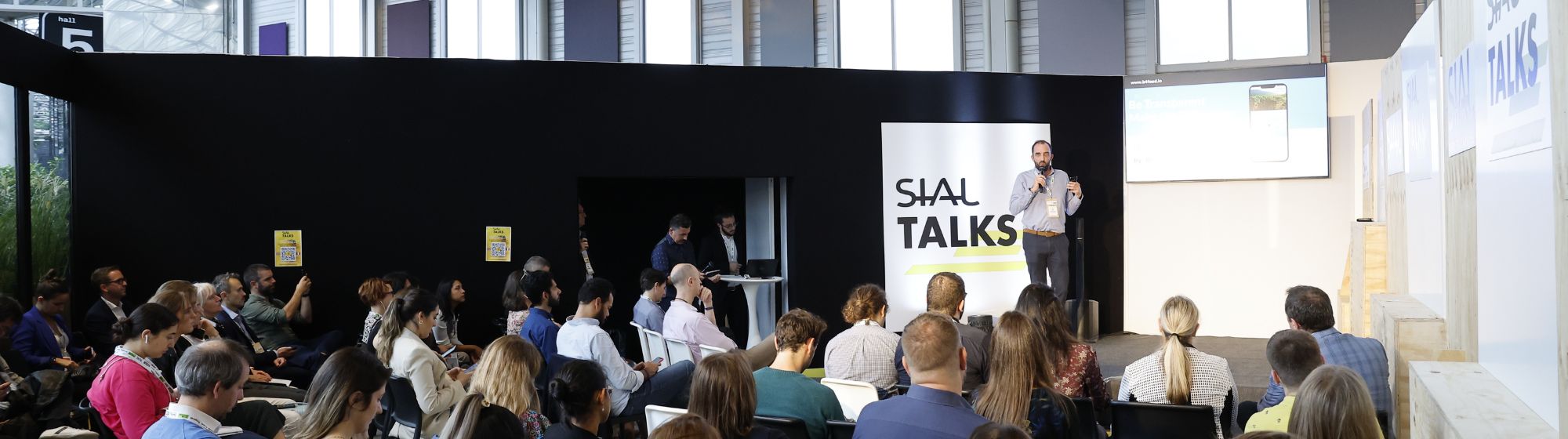 SIAL Talks conference with a speaker on stage and an attentive audience in a black room