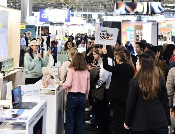 Groupe de visiteurs assistant à une visite guidée SIAL sur un stand avec une personne tenant un panneau "SIAL Guided Tour".