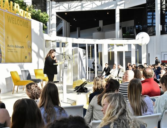 Conference with Audrey Ashworth speaking to an attentive audience in a bright, modern open space.