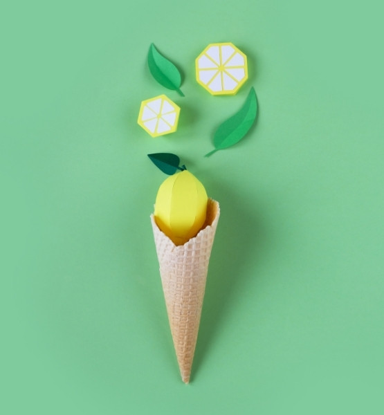 Cornet de glace avec citron en papier et feuilles vertes sur fond vert pastel.