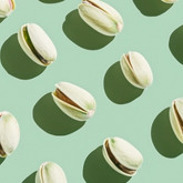 Pistaches ouvertes disposées en motif régulier sur un fond vert, avec ombres marquées.