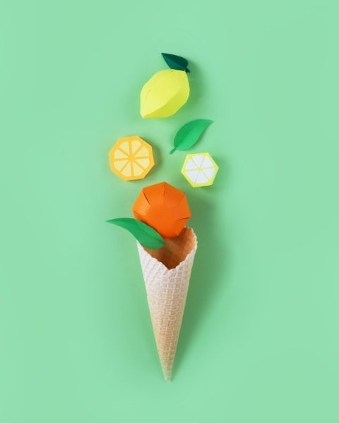 Ice cream cone with colorful paper fruits (lemon, orange) in a minimalist style on a pastel green background
