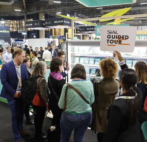 Groupe de visiteurs assistant à une visite guidée au salon SIAL, rassemblés près du point de départ avec un panneau "SIAL Guided Tour" en arrière-plan.