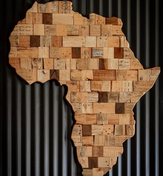 Carte en bois représentant le continent africain, constituée de plusieurs blocs de différentes nuances, accrochée à un mur métallique.