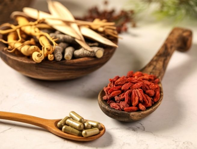 Cuillères en bois contenant des gélules et des baies séchées sur fond clair.