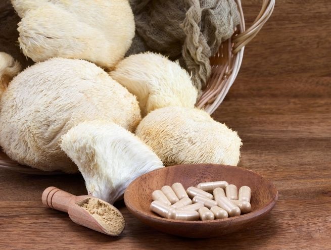 Lion's Mane mushrooms and adaptogenic capsules with powder in a wooden spoon, displayed on a wooden background.