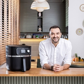 A smiling chef in the kitchen with a black air fryer on the countertop