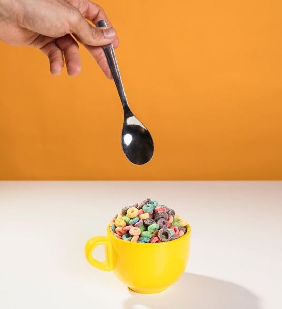 Hand scooping crunchy and colorful cereal with a spoon from a cup