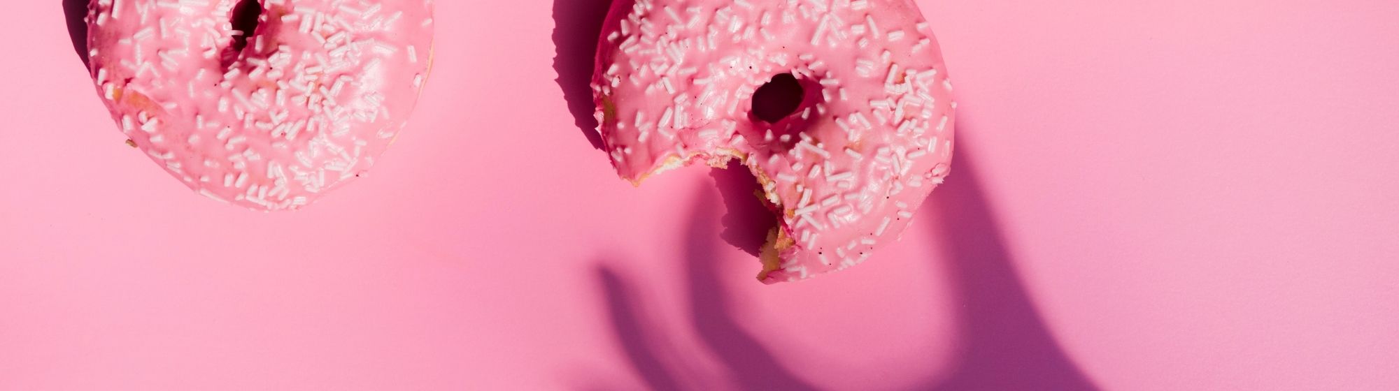 Pink frosted donuts with white sprinkles on pink background