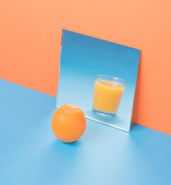 Orange entiere et verre de jus devant miroir sur fond orange et bleu