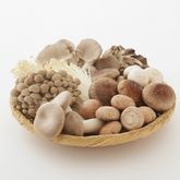 Assortment of fresh mushrooms arranged in a basket on a light background.