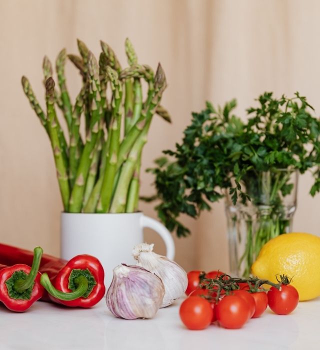 Légumes frais comprenant tomates, ail, asperges, citron et persil sur un plan de travail.