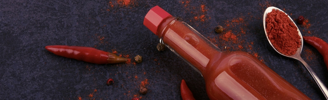 Sauce pimentée avec piment et poudre de piment sur un fond sombre.