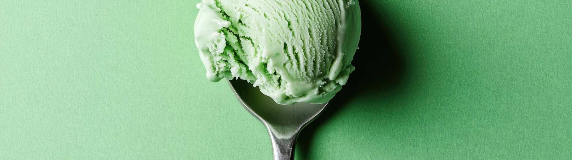 Green ice cream scoop on a spoon with wide framing on a green background.
