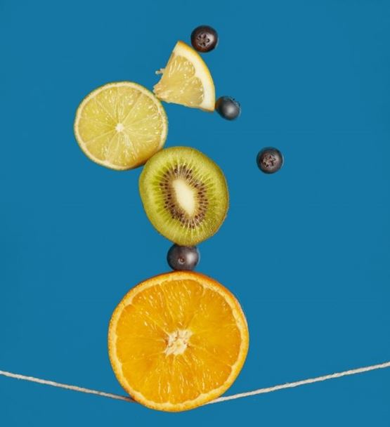 Fruits arranged in balance with orange, kiwi, lemon and blueberries on a blue background.