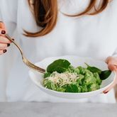 Personne tenant une assiette de salade verte avec une fourchette, vue rapprochée.