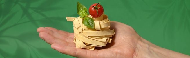 Pâtes garnies de tomates cerises et basilic, sur fond vert lumineux.