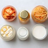 Pot de nourriture fermentée sur fond neutre, avec ingrédients en vue.