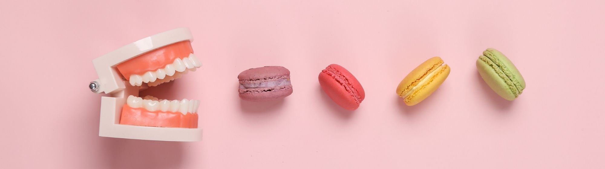 Dentier ouvert facing des macarons colorés sur fond rose, illustration consommation sucre et santé dentaire