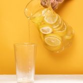 Verre d’eau avec citron en cours de service sur fond jaune, illustration hydratation saine et rafraîchissante