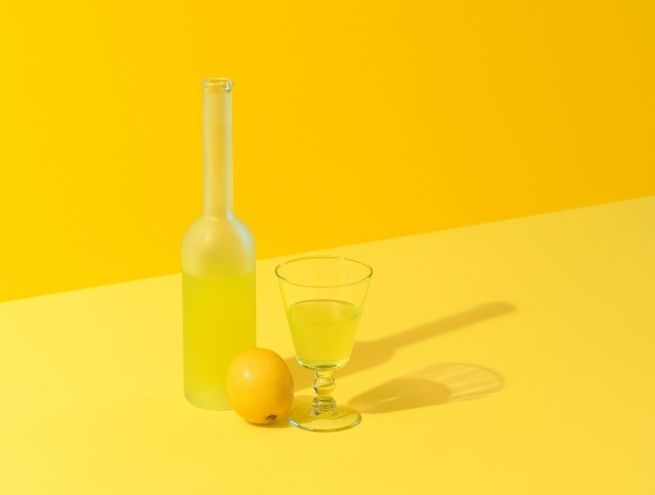 Homemade lemonade glass with whole lemon on bright yellow background