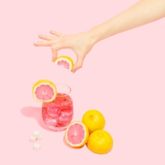 Main versant boisson rose avec agrumes sur fond pastel