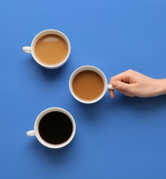 Three cups of light and dark coffee on blue background, hand holding a cup.