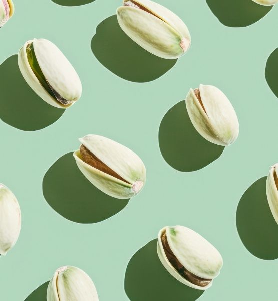Pistaches décortiquées disposées de manière graphique sur un fond vert clair