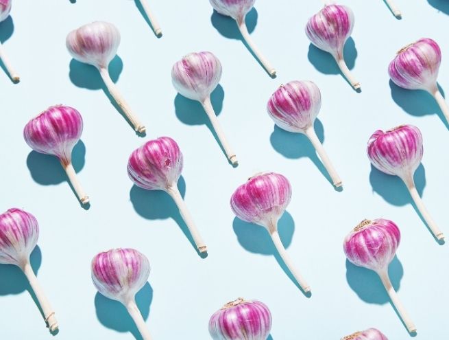 Pattern of purple garlic bulbs arranged in repetition on a light blue background