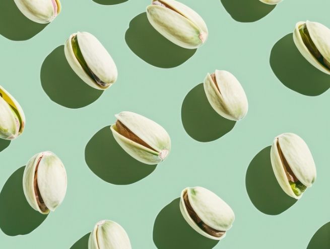 Pattern of open pistachios spread across a pastel green background.